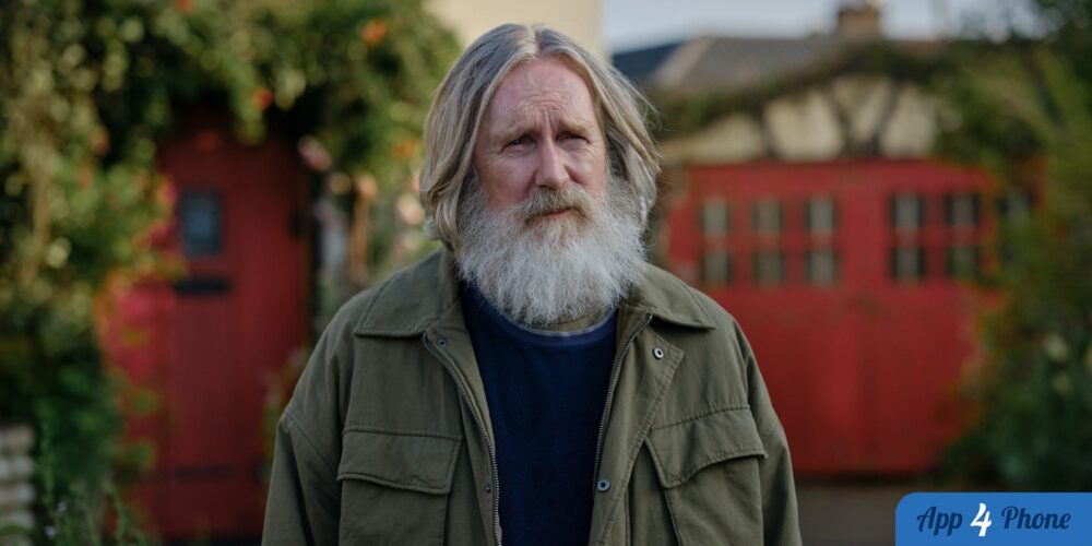 Portrait rapproché d’un homme barbu devant une maison rouge