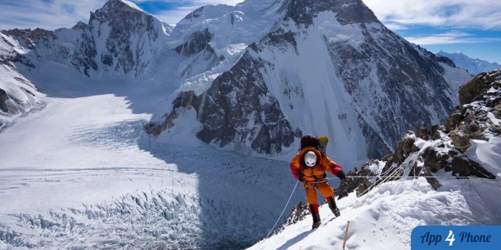 Alpiniste en combinaison orange escaladant une montagne enneigée
