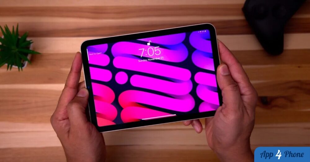 iPad mini tenu à la main, écran allumé sur une table en bois